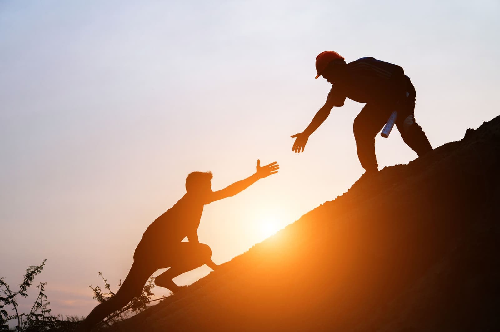Two travellers helping each other up a hill at sunrise